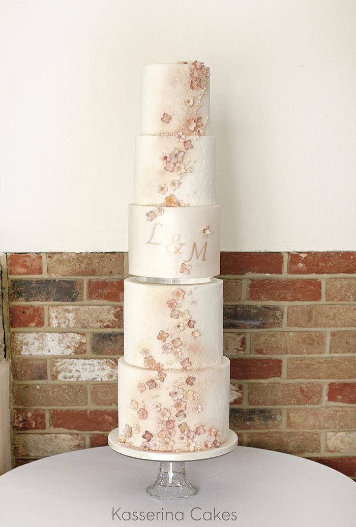 Tall stacked wedding cake with muted blossoms and monogram