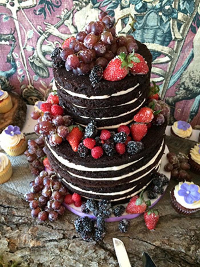 A naked chocolate cake with fresh fruit. 