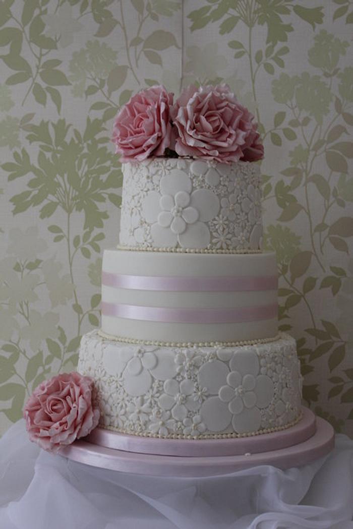 A three tier wedding cake with 2 embossed tiers and flowers