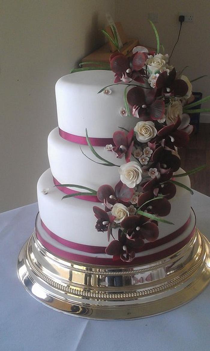 Tumbling burgundy orchid spray with cream roses, waxflower and grasses