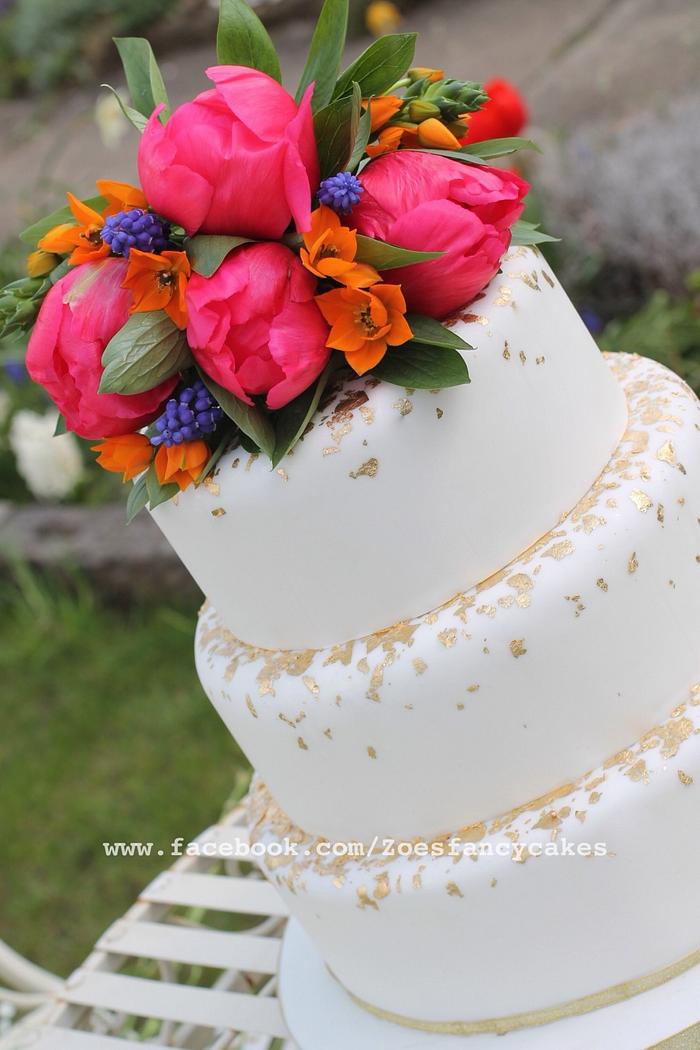 Gold and white wedding cake with real flowers.