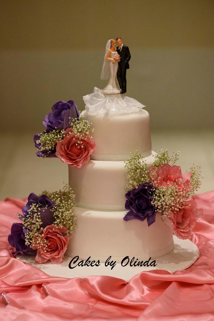 Simple wedding cake with pink and purple sugar roses with a hint of fresh babies breath