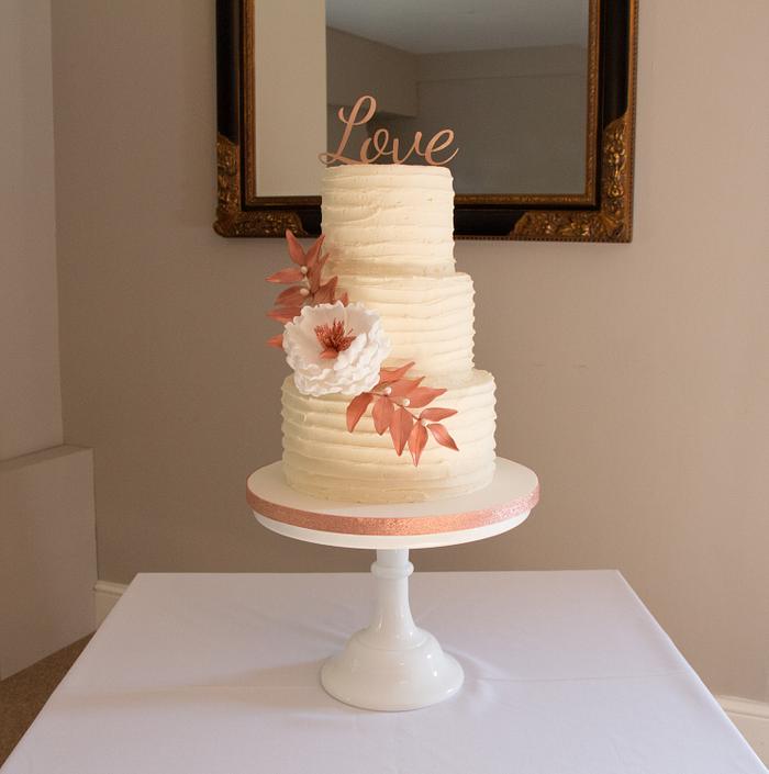 Buttercream wedding cake with open peony and rose gold foliage