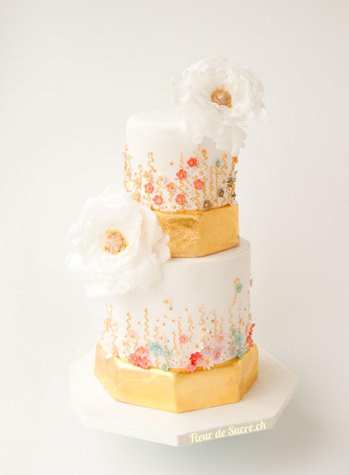 a gold wedding cake with pastel blossoms and white peonies