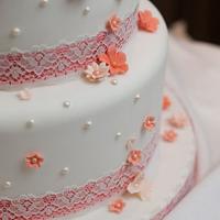Coral blossom and pearl cascade wedding cake with coral ribbon and lace overlay