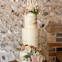 Semi naked tiered cake with fresh flowers and large topper