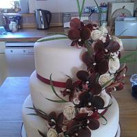 Tumbling burgundy orchid spray with cream roses, waxflower and grasses