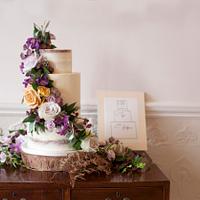 Semi-naked wedding cake with purple and amber fresh flowers