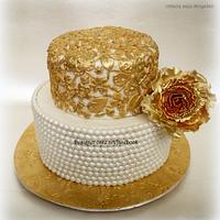 A simple vintage cake with gold lace work and sugar pearls .