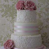 A three tier wedding cake with 2 embossed tiers and flowers