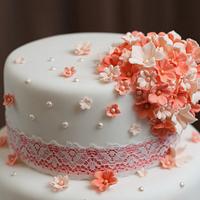 Coral blossom and pearl cascade wedding cake with coral ribbon and lace overlay