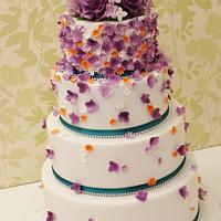 Purple and orange Cascading hydrangea and blossom wedding cake with a rose topper