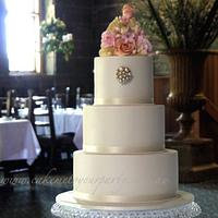 Three tiered ivory wedding cake with pearls and floral bouquet topper. 